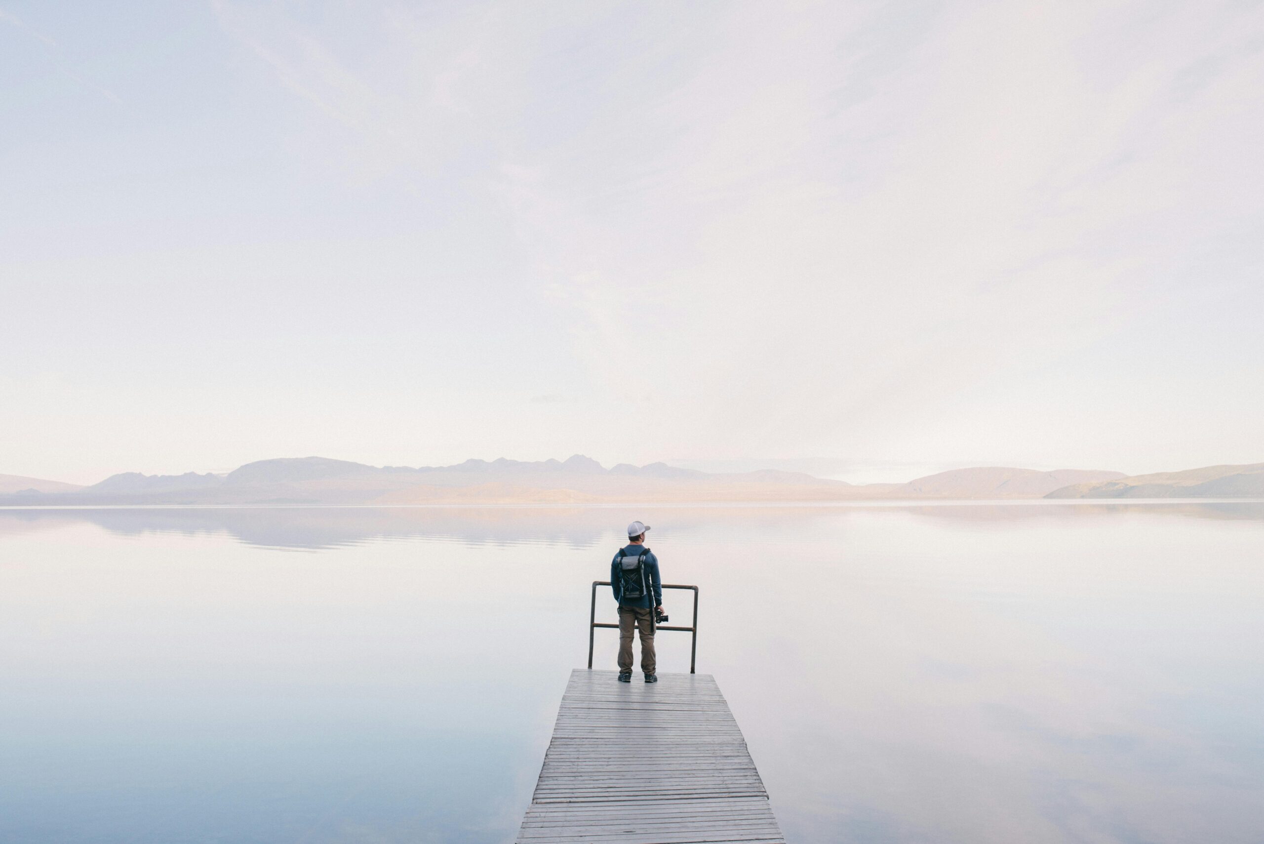 A solitary traveler stands on a dock enjoying the serene water view